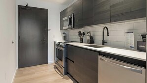 A modern kitchen with a built-in oven, microwave, and dishwasher, featuring dark cabinetry and a light countertop. - Landing | Modern 1BD, Courtyard, Pool (Orlando)