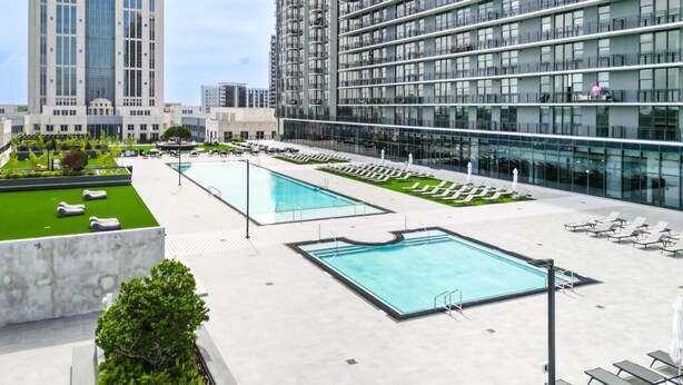 A rooftop pool area with multiple swimming pools, lounge chairs, and a view of surrounding high-rise buildings. - Landing | Modern 1BD, Courtyard, Pool (Orlando)