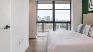 A bedroom with a large window, a bed, and a view of a cityscape. - Landing | Modern 1BD, Courtyard, Pool (Orlando)