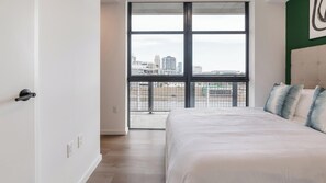 Ein Schlafzimmer mit großem Fenster, einem Bett und Blick auf eine Stadtlandschaft.