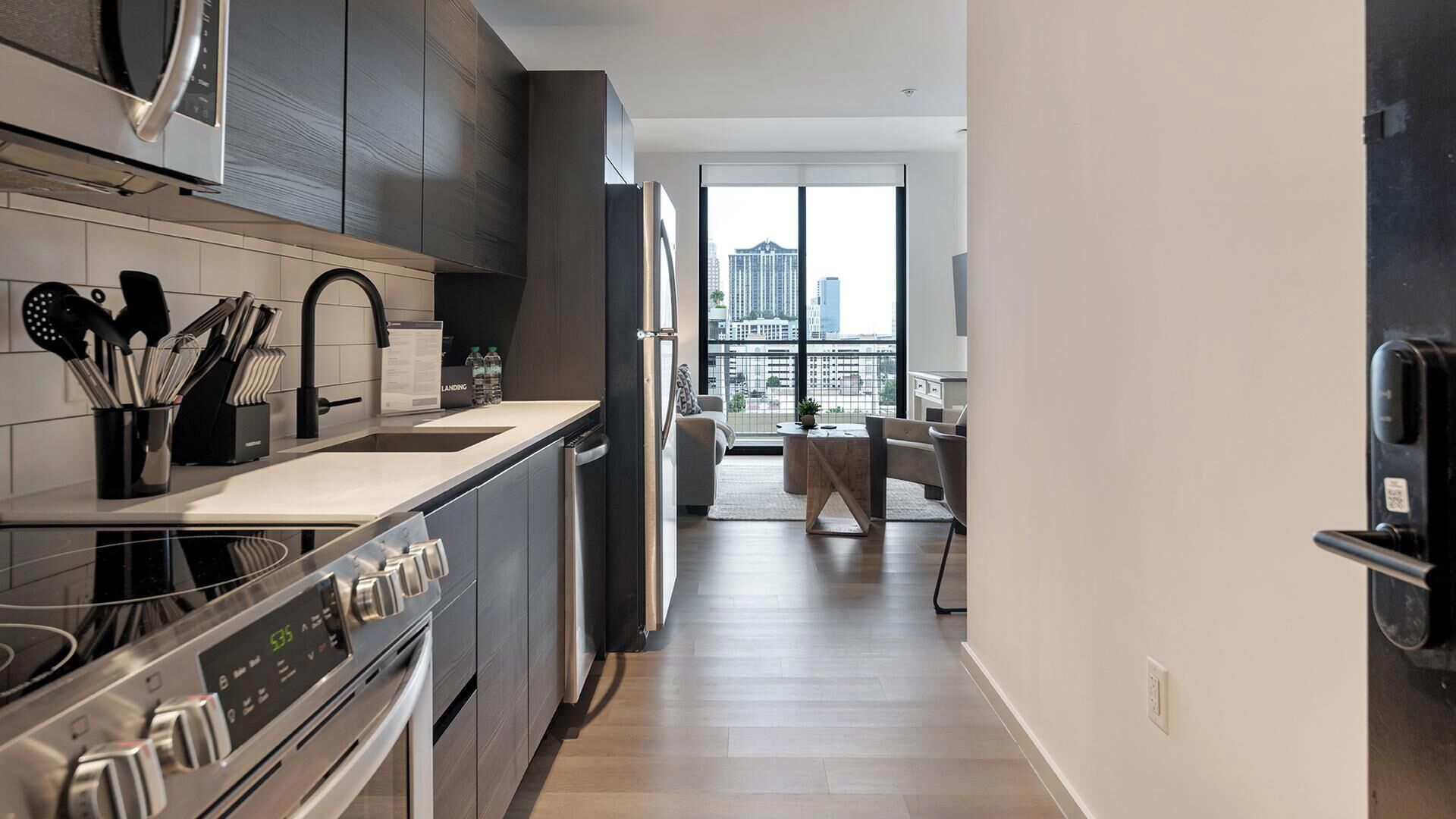 A modern kitchen with a built-in oven, a stainless steel range hood, and a large window offering a view of the cityscape.