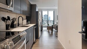 A modern kitchen with a built-in oven, a stainless steel range hood, and a large window offering a view of the cityscape. - Landing | Stylish 1BD, Pool, Courtyard (Orlando)