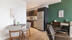 A modern kitchen with a refrigerator, microwave, and wooden cabinets. There is a dining area with a round table and two chairs. - Landing | Stylish 1BD, Rooftop Lounge, Gym (Orlando)