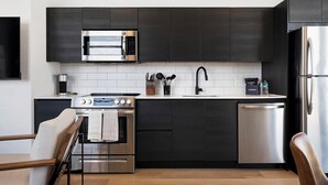A modern kitchen with dark cabinetry, a stainless steel microwave, a built-in oven, a dishwasher, and a sink with a faucet. - Landing | Stylish 2BD, Courtyard, Pool (Orlando)
