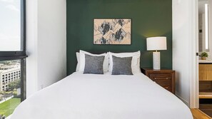 Une chambre à coucher avec un lit, des oreillers, une table de chevet, une lampe et un tableau au mur.