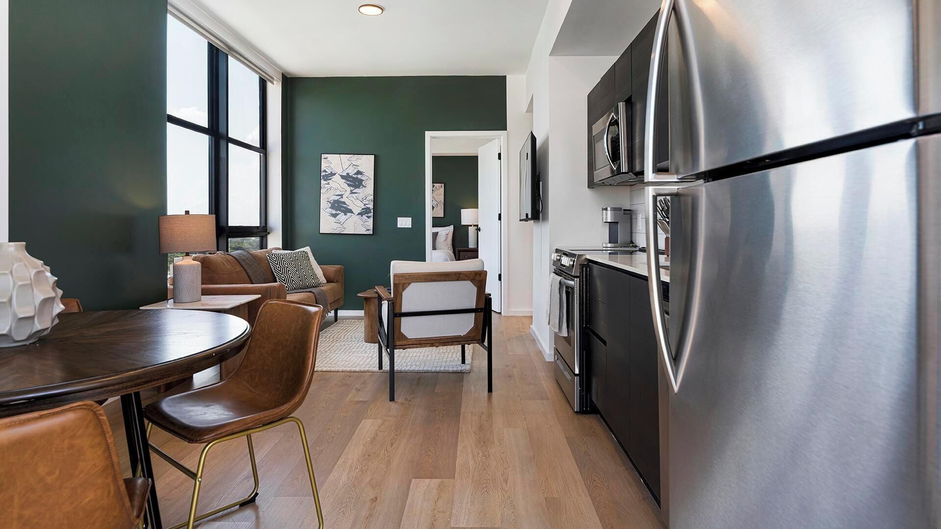 Une cuisine moderne dotée d’un réfrigérateur en acier inoxydable, d’un plancher en bois et d’un coin repas avec une table et des chaises.