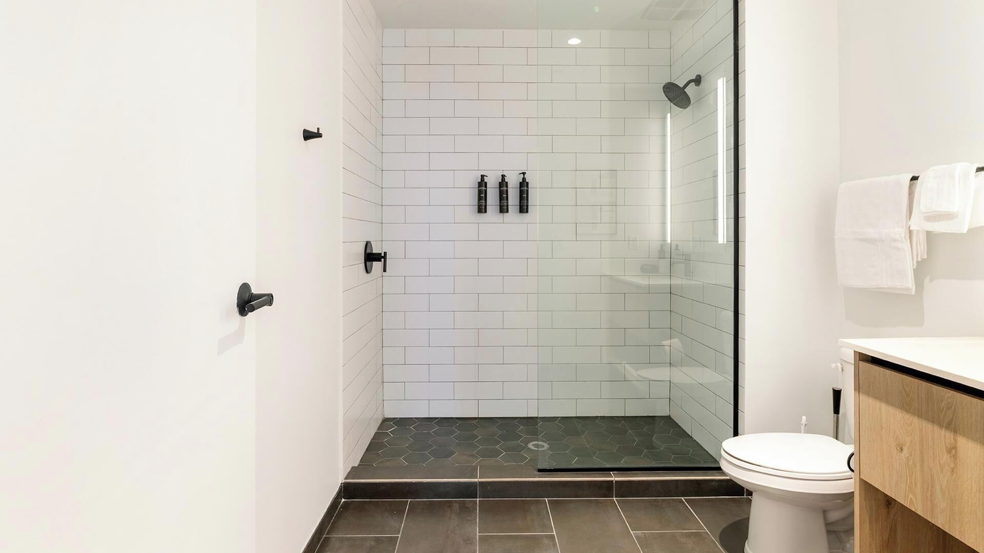 Een moderne badkamer met een douchecabine van glas, witte betegelde muren en een houten wastafelmeubel.