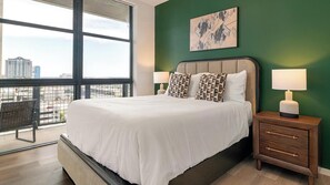 A hotel room with a large bed, two bedside lamps, a city view, and a green accent wall. - Landing | Amazing 2BD, Pool, Gym (Orlando)