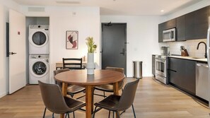 A modern kitchen with stainless steel appliances, a dining area with a round table and chairs, and a laundry room with stacked washers and dryers. - Landing | Amazing 2BD, Pool, Gym (Orlando)