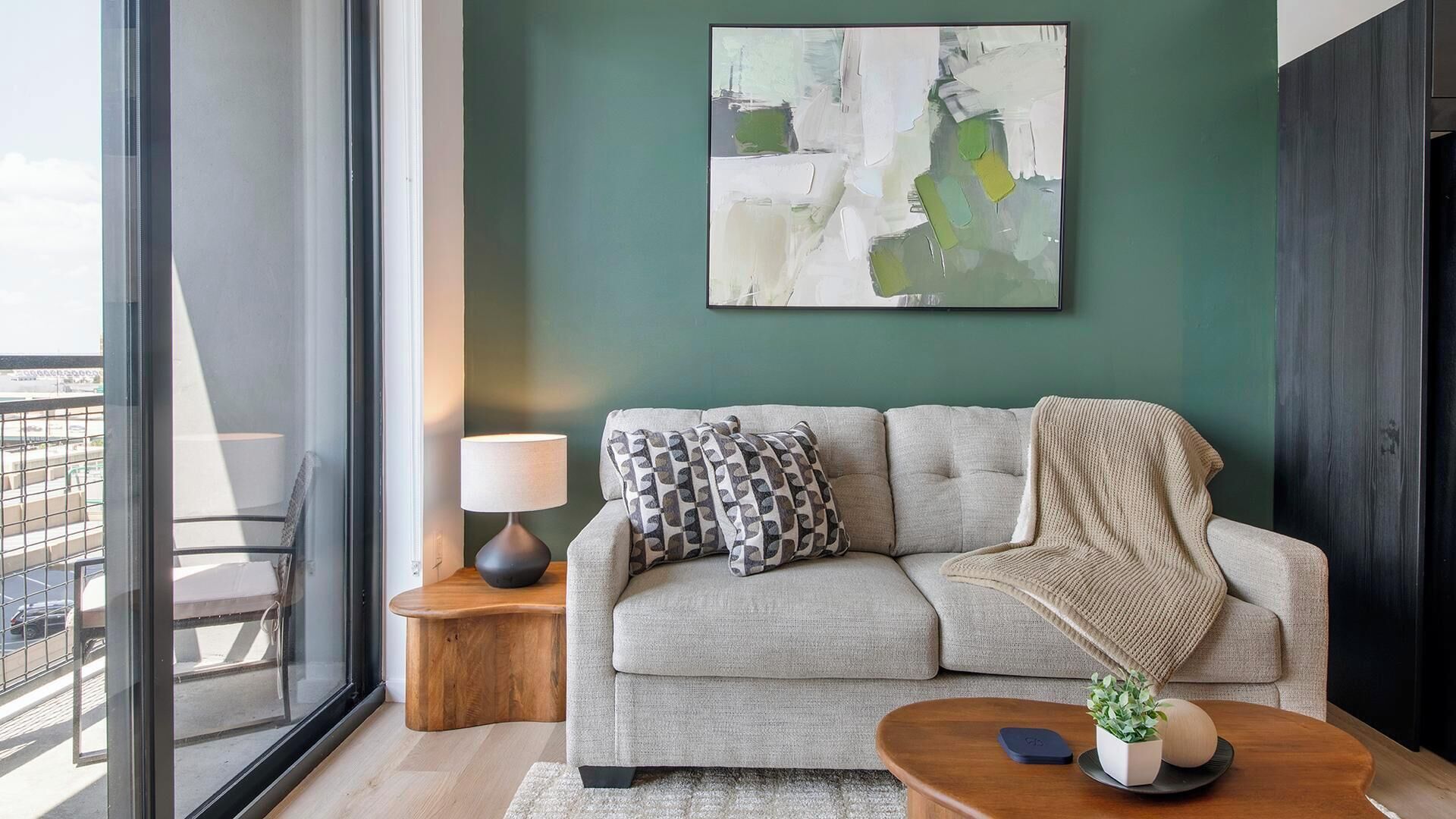 Ein modernes Wohnzimmer mit einer Couch, einem Beistelltisch mit Lampe, einem Couchtisch mit Pflanze und einem großen abstrakten Gemälde an der Wand.