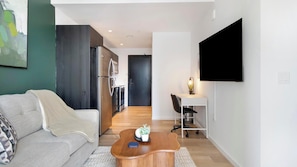 A modern living space with a sofa, a wooden coffee table, a TV, and a kitchen area. - Landing | Incredible 1BD, Gym, Rooftop Lounge (Orlando)