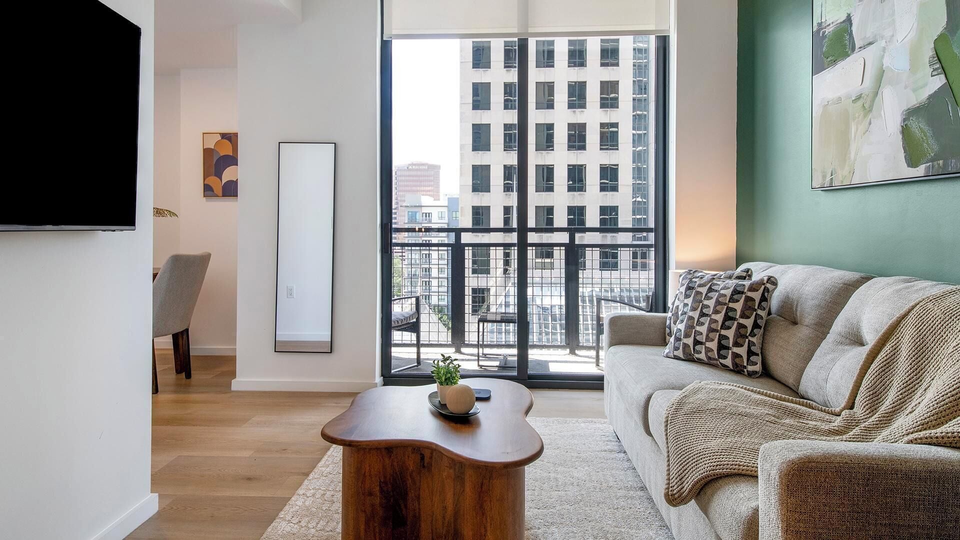 Ein modernes Wohnzimmer mit einer Couch, einem Couchtisch, einem Fernseher und einem großen Fenster mit Blick auf die Stadt.