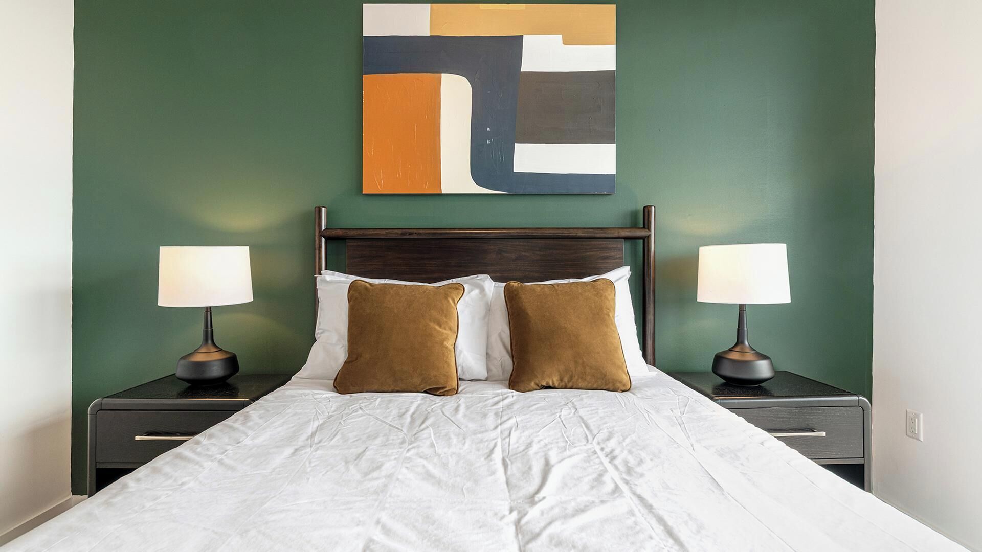 A hotel room with a bed, two bedside tables, two lamps, and a wall art piece.