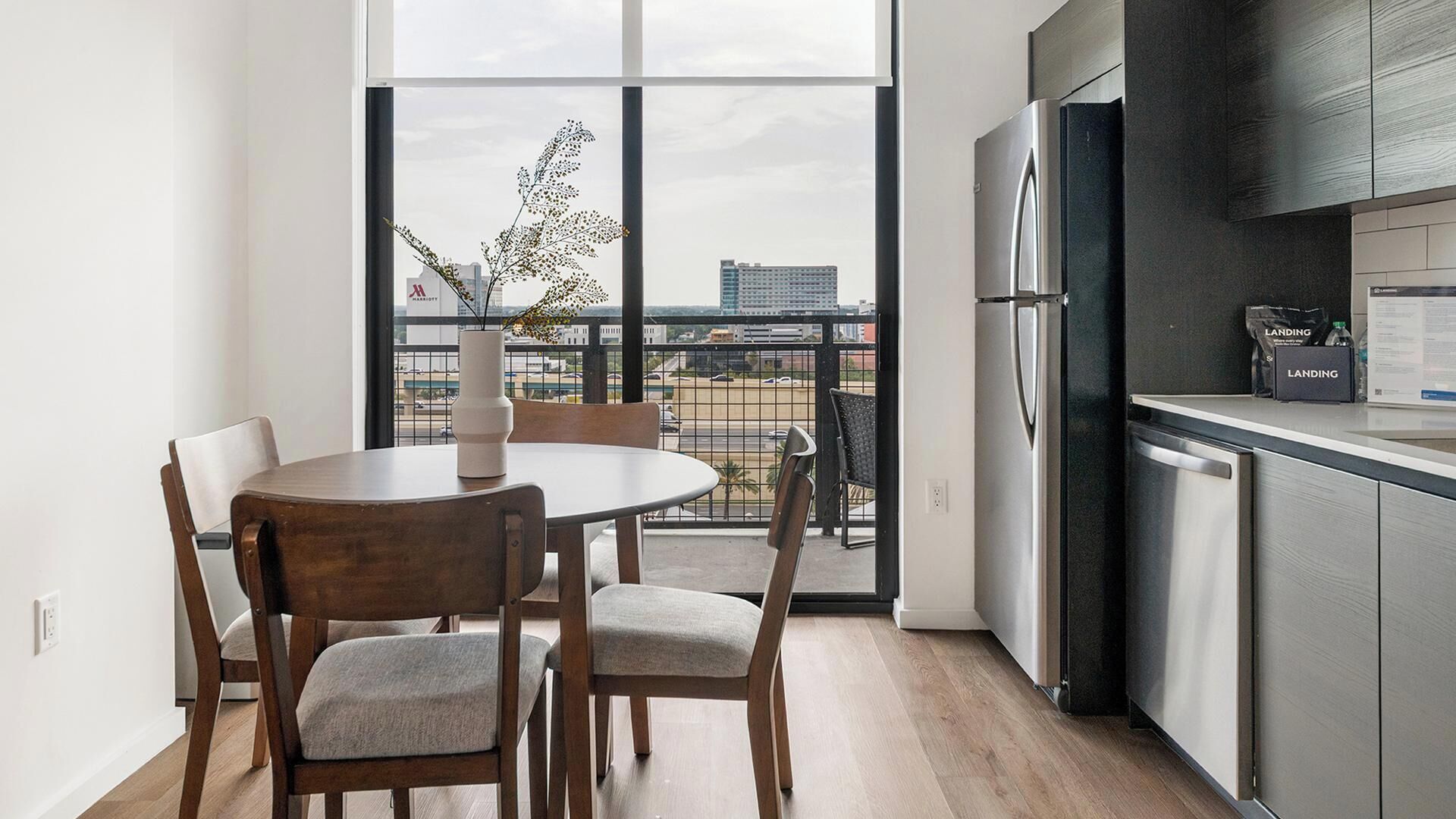 A modern kitchen with a large window, a dining area with two chairs, and a refrigerator.