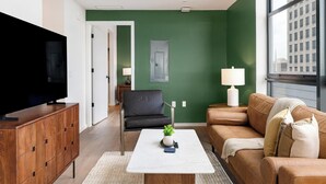 A living room with a television, a sofa, a coffee table, and a green accent wall. - Landing | Beautiful 2BD, Gym, Pool (Orlando)