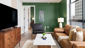 A living room with a television, a sofa, a coffee table, and a green accent wall. - Landing | Beautiful 2BD, Gym, Pool (Orlando)