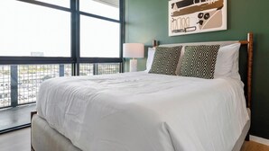 Hotellihuone, jossa on suuri sänky, ikkunasta avautuva näkymä ja seinälle asennettu lamppu.