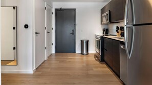 A modern kitchen with stainless steel appliances, a trash can, and a door leading to another room. - Landing | Stylish Studio, Pool, Rooftop Lounge (Orlando)