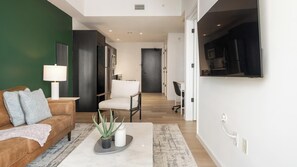 A modern living room with a sofa, a coffee table with a plant, and a TV mounted on the wall. - Landing | Stylish 1BD, Gym, Pool (Orlando)