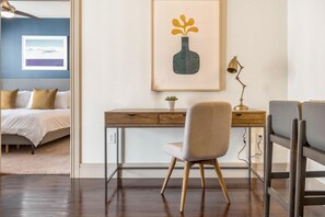 Une chambre à coucher avec un lit, un bureau avec une chaise, un tableau encadré et une petite plante.