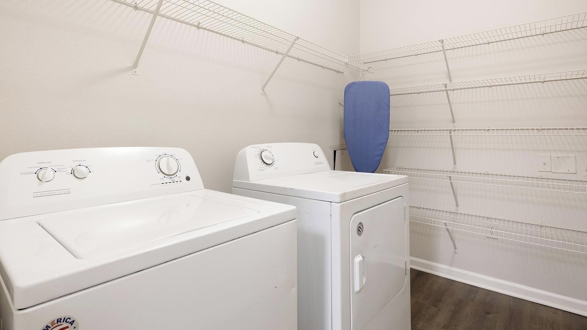Une buanderie équipée de deux machines à laver et de deux sèche-linge blancs, d’un étendoir bleu et d’étendoirs métalliques fixés aux murs.