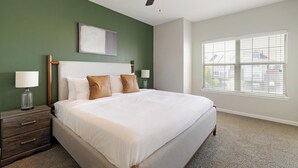 Ein Hotelzimmer mit einem großen Bett, zwei Nachttischen, einem Fenster mit Jalousien und einer Wand in Grünton.