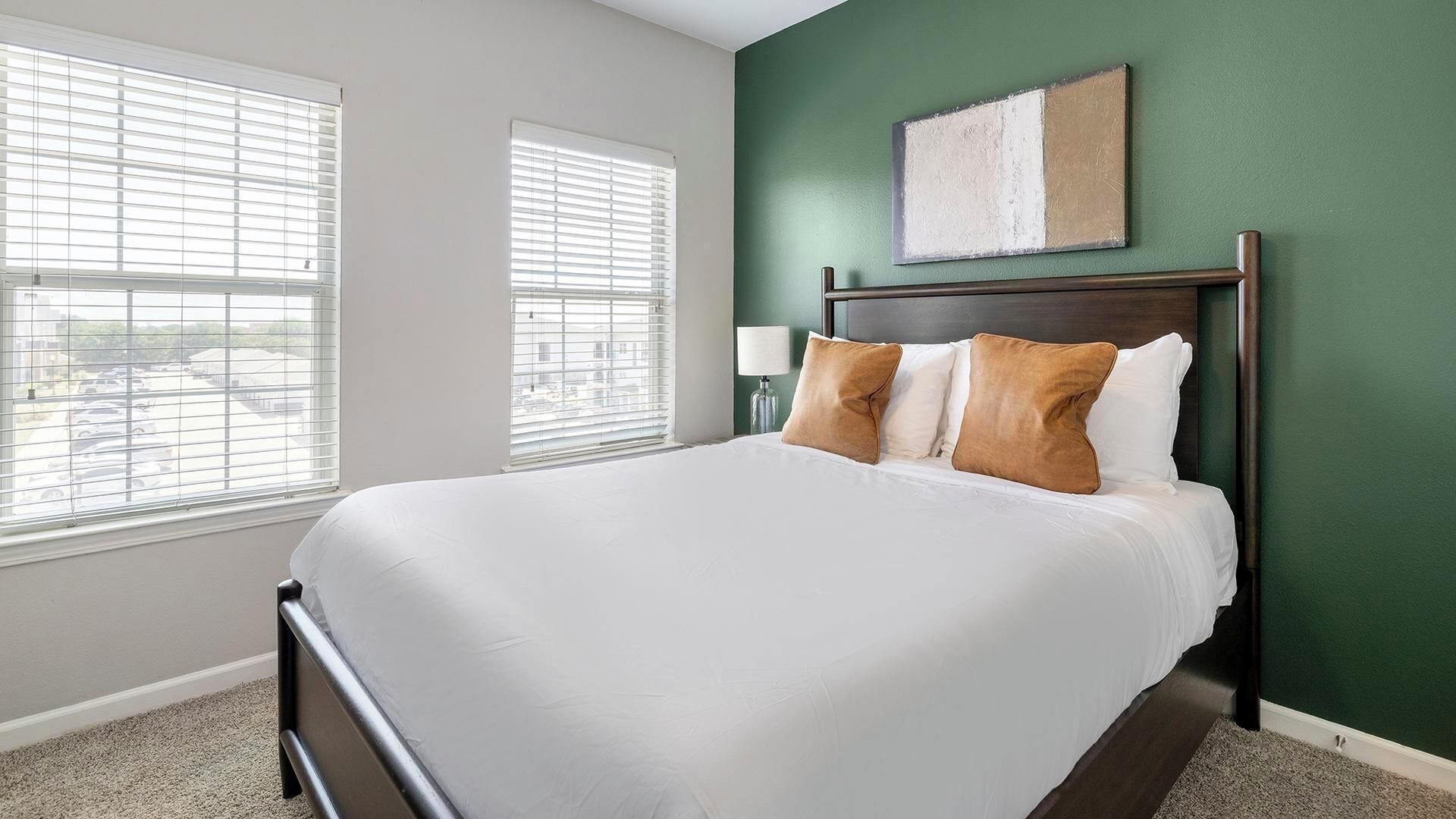 A hotel room with a large bed, two bedside lamps, and a view through the windows.