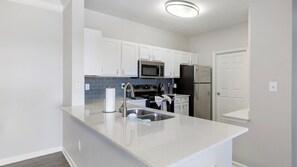 Une cuisine moderne avec des meubles blancs, un réfrigérateur en acier inoxydable, un four à micro-ondes et un évier.