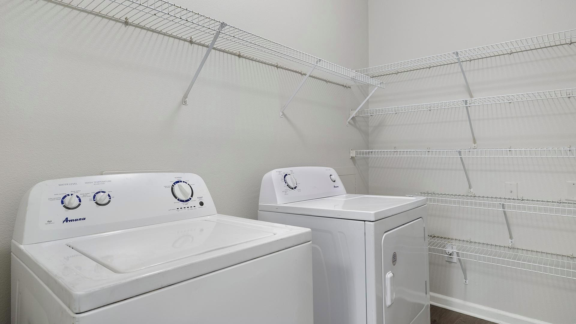 A laundry area with two white Amana washing machines and metal drying racks.