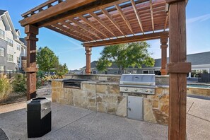 Un espace barbecue extérieur agrémenté d’un mur en pierre, d’un gril et d’une structure en forme de pergola.