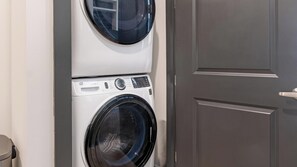 Un appareil combiné lave-linge et sèche-linge, placé verticalement contre un mur, avec une porte à proximité.