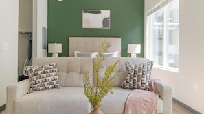 Ein Wohnzimmer mit einer Couch, zwei Lampen, einer Vase mit Grünpflanzen und einem Gemälde an der Wand.