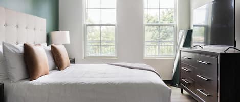 A hotel room with a large bed, a dresser, a television, and two windows.