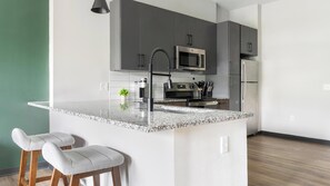 Eine moderne Küche mit Granit Arbeitsplatte, Edelstahlgeräten und einer kleinen Kochinsel mit Barhocker.