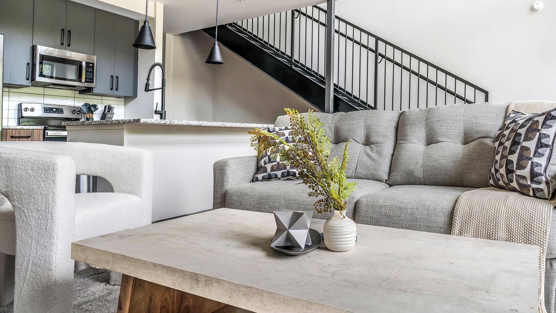 Ein modernes Wohnzimmer mit einem grauen Sofa, einem Couchtisch und einer Küche im Hintergrund.