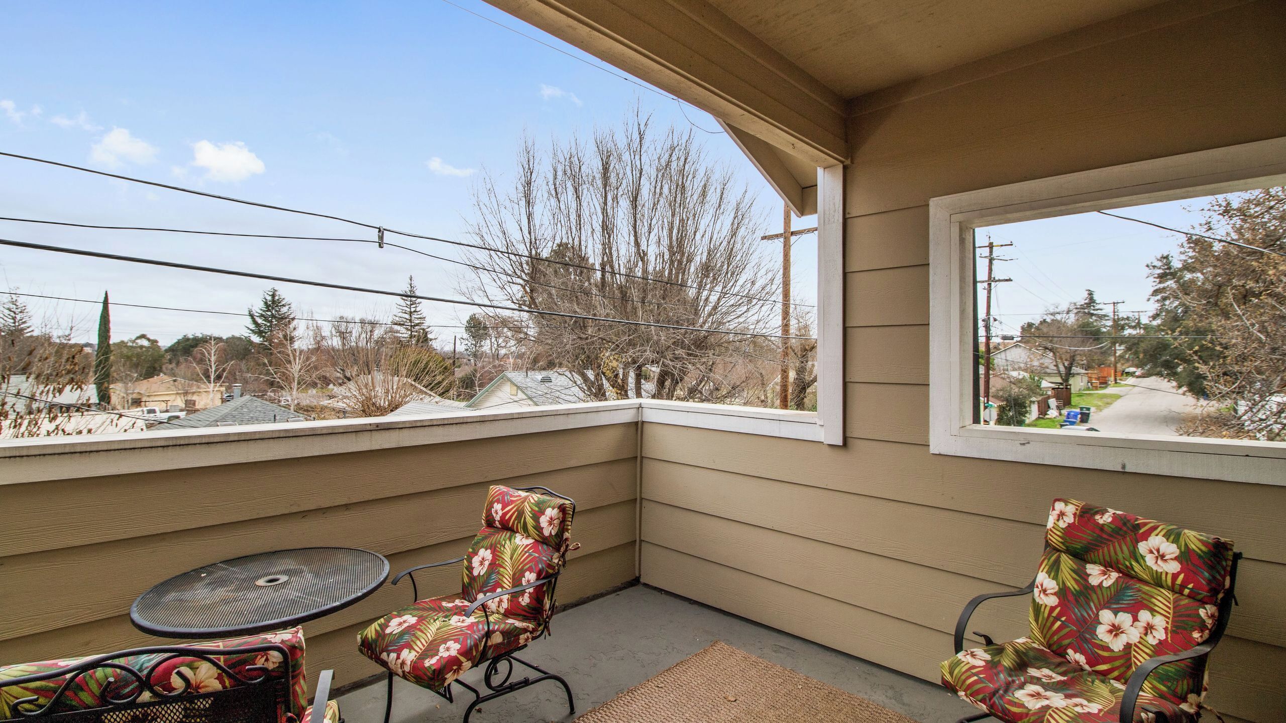 A covered outdoor seating area with two chairs and a table, overlooking a residential neighborhood.