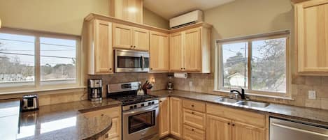 Una cocina con armarios de madera, estufa de acero inoxidable, microondas y lavavajillas.