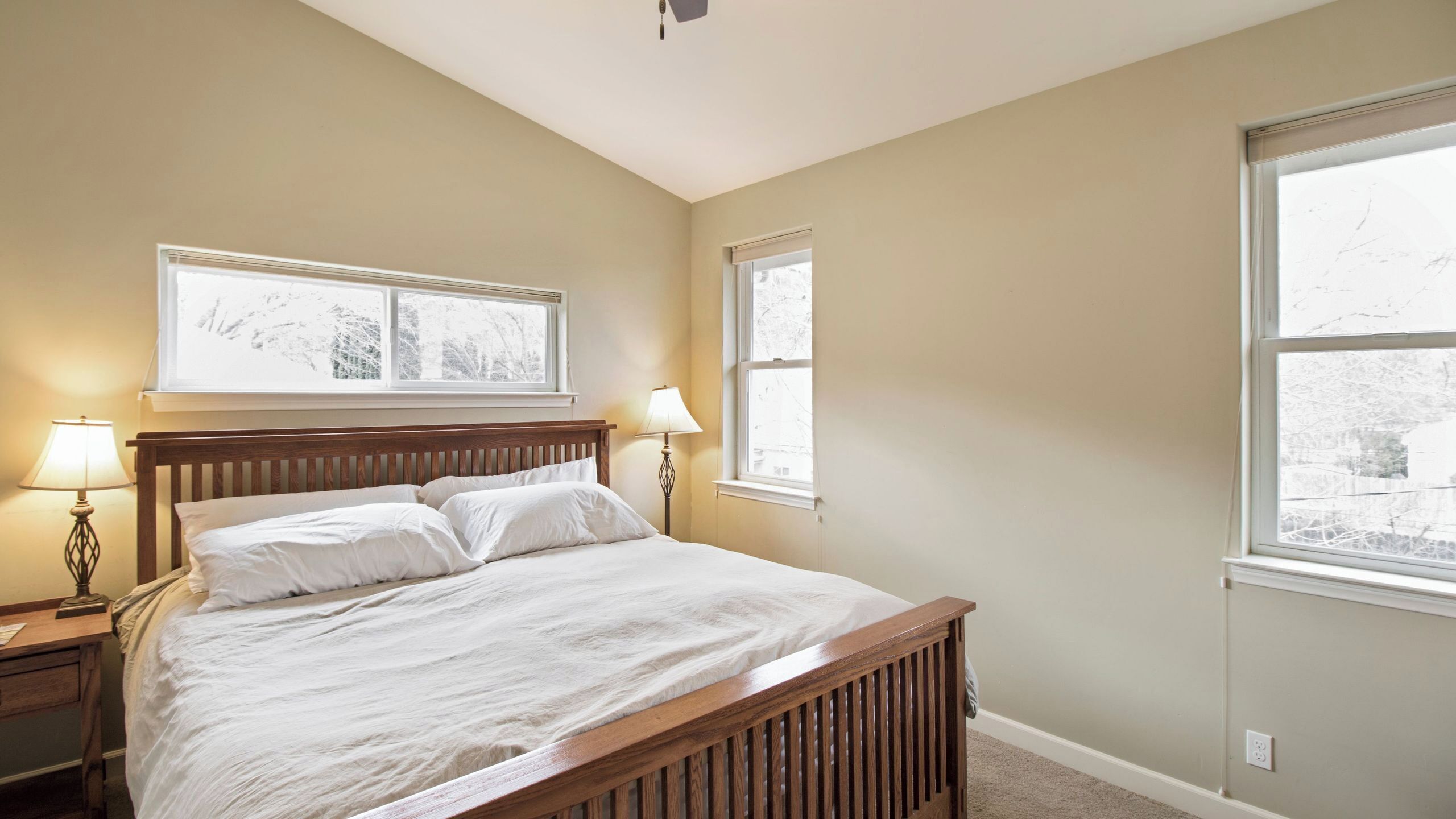 A bedroom with a wooden bed, two bedside lamps, and a window with a view of trees.