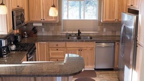 Cocina con encimeras de granito, armarios de madera, electrodomésticos de acero inoxidable e iluminación colgante.