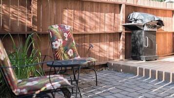 An outdoor patio with two chairs, a table, and a grill.