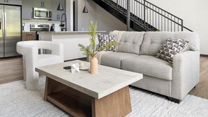 A modern living room with a sofa, a coffee table, and a kitchen in the background. - Landing | Spectacular 1BD, Gym, Courtyard (Atlanta)