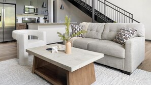 A modern living room with a sofa, a coffee table, and a kitchen in the background. - Landing | Spectacular 1BD, Gym, Courtyard (Atlanta)
