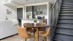 Eine moderne Küche mit Edelstahlgeräten, ein Essbereich mit Holztisch und Stühlen sowie eine Treppe mit Metallgeländern.