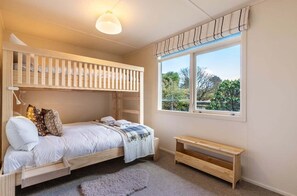 Ein Schlafzimmer mit einem Etagenbett, einem Einzelbett, einem Fenster mit Ausblick und einer kleinen Holzbank.