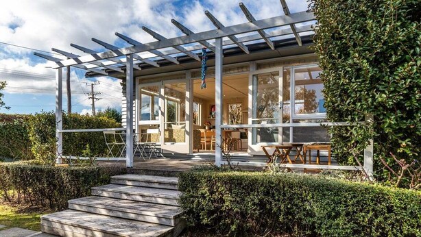 Ein modernes Haus mit überdachter Terrasse, einer Holztreppe und einem gepflegten Garten.