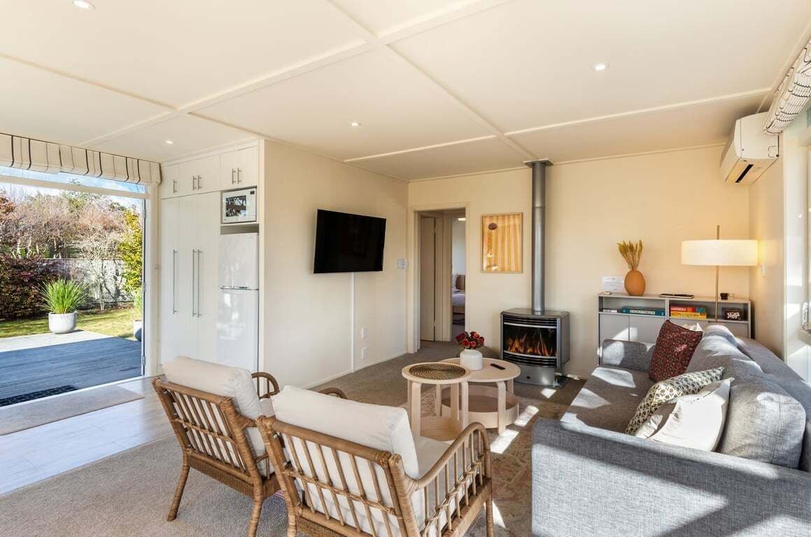 A modern living room with a sofa, two chairs, a fireplace, a television, and a large window overlooking a garden.