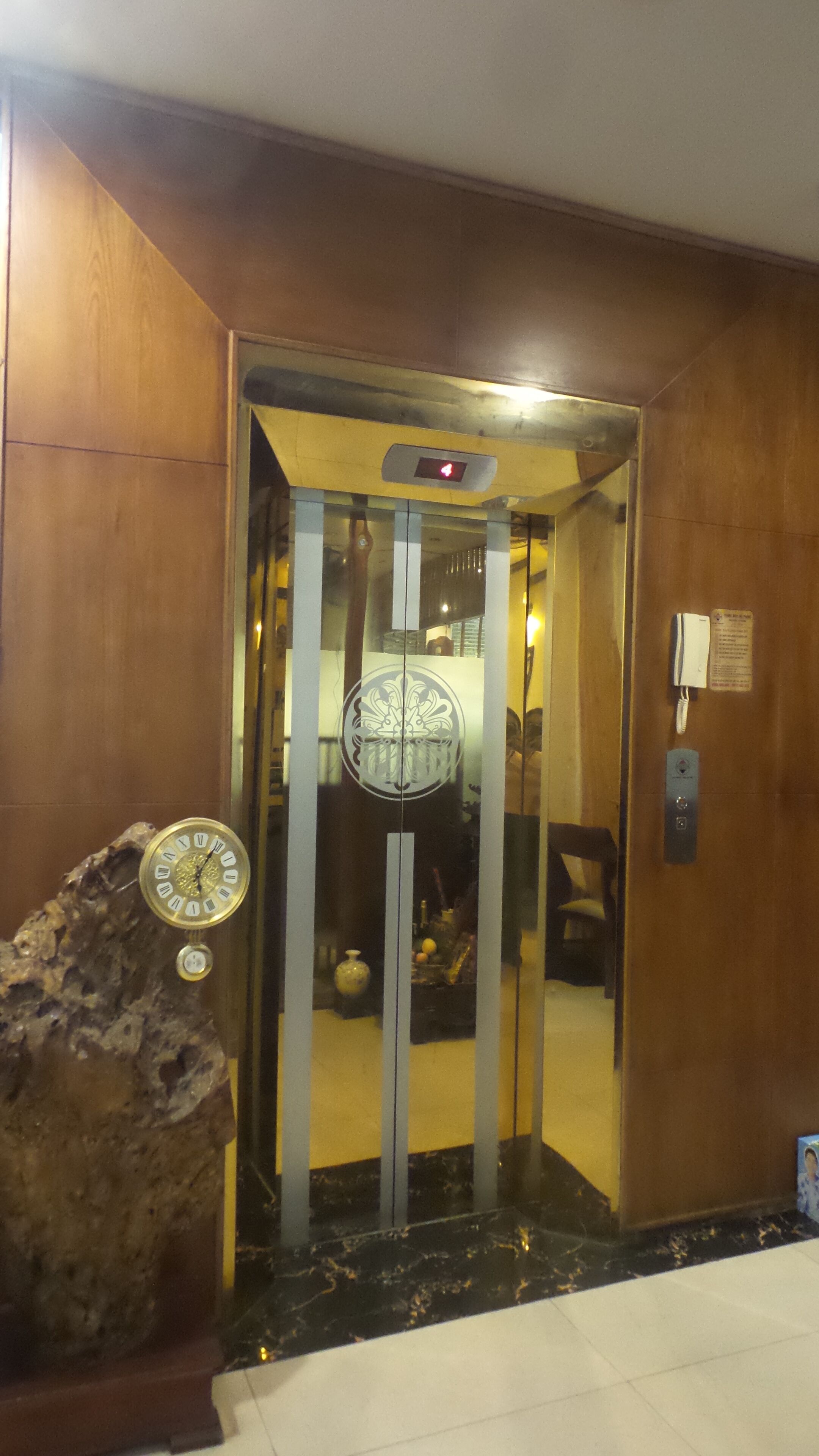 Um elevador com porta de vidro, um relógio e um telefone na parede.