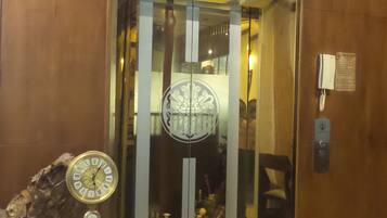 Um elevador com porta de vidro, um relógio e um telefone na parede.