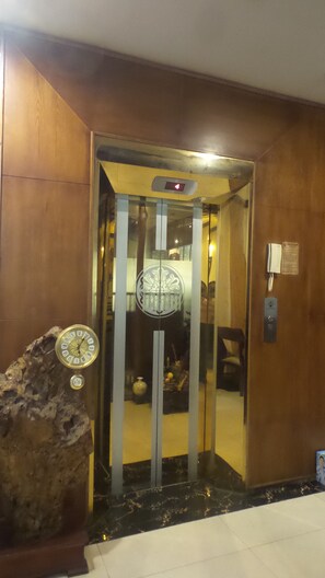 Um elevador com porta de vidro, um relógio e um telefone na parede.