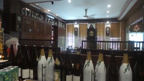 A bar area with bottles and glasses, wooden shelves, and a ceiling fan.